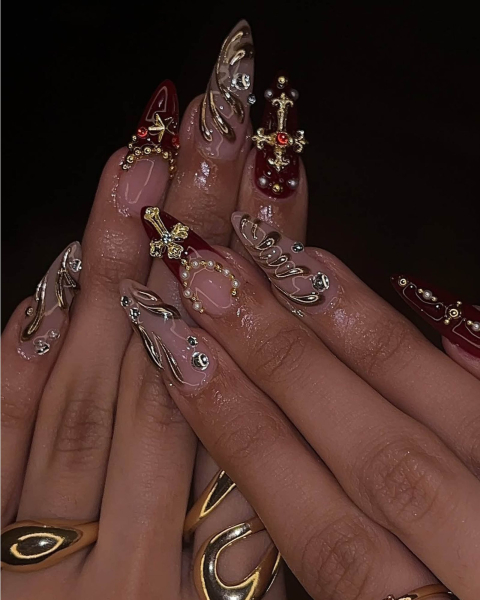Maroon and nude glossy nails with gold and silver puffy crosses.